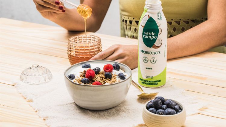 Bebida probiótica Verde Campo sabor coco ao lado de tigela com granola, frutas vermelhas e mel.
