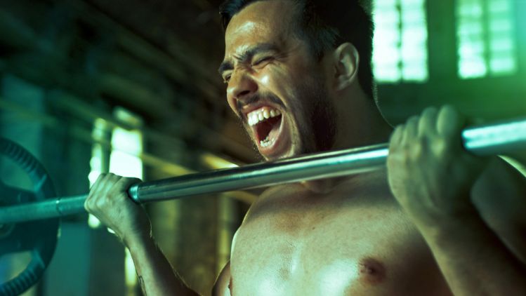 Pessoa realiza rosca bíceps com barra durante treino de musculação na academia.