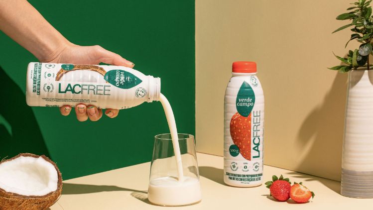 Bebida lacfree Verde Campo sendo servida em copo de vidro, com morangos e coco como acompanhamento.
