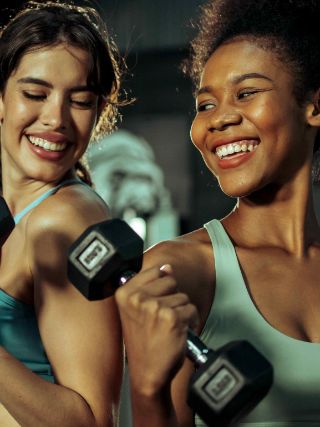Duas pessoas levantam halteres durante treino de braço em academia.